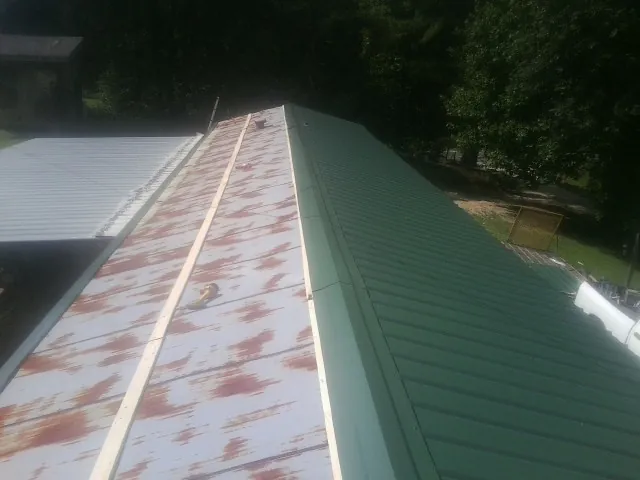 Old rusted panels beside newly installed green metal roofing — Wind Damage Roof Repair by Roofing Brothers in Manchester
