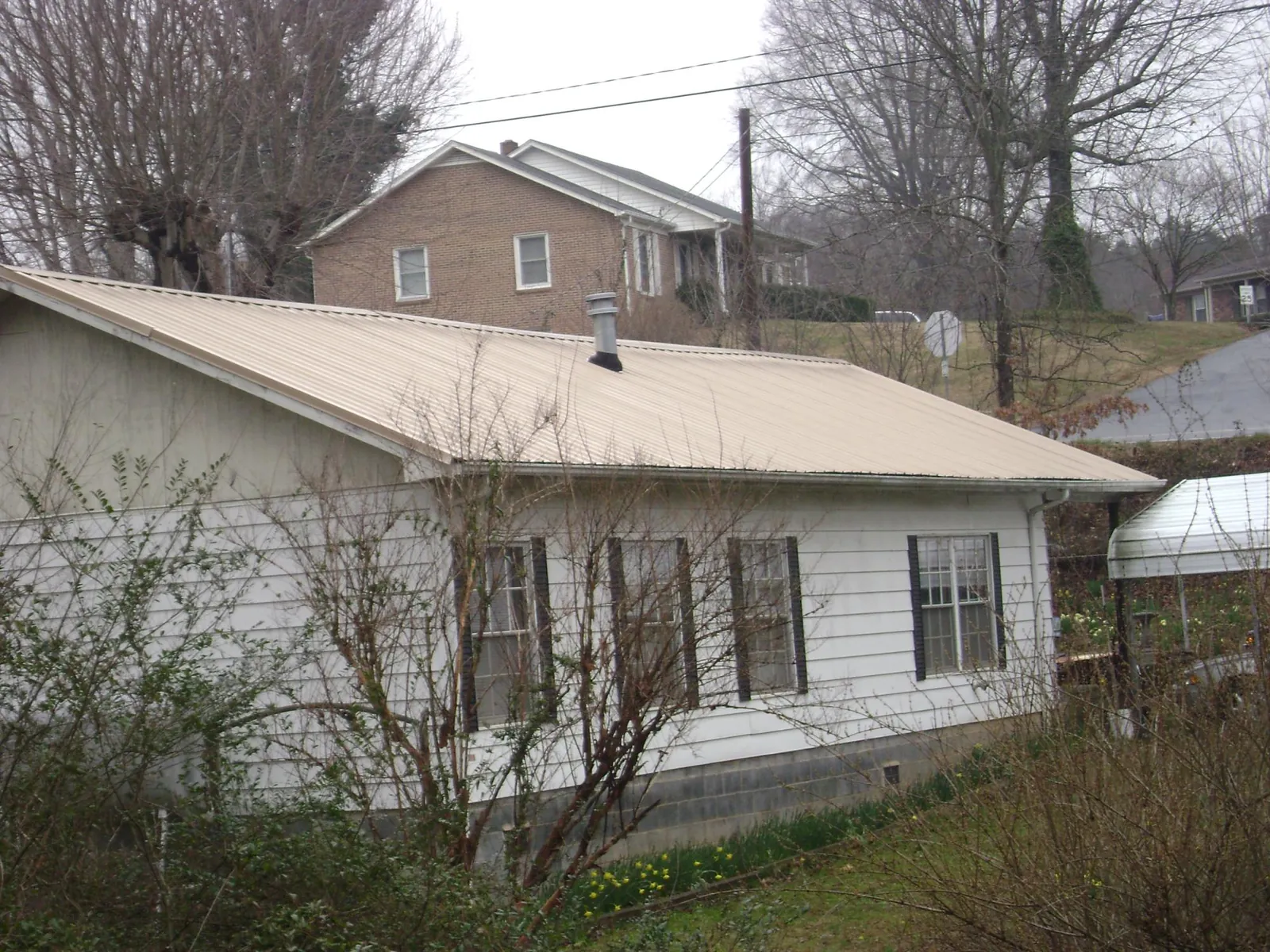 Tan metal roof on a white sided house set into a hillside — Commercial Roofing by Roofing Brothers in Manchester