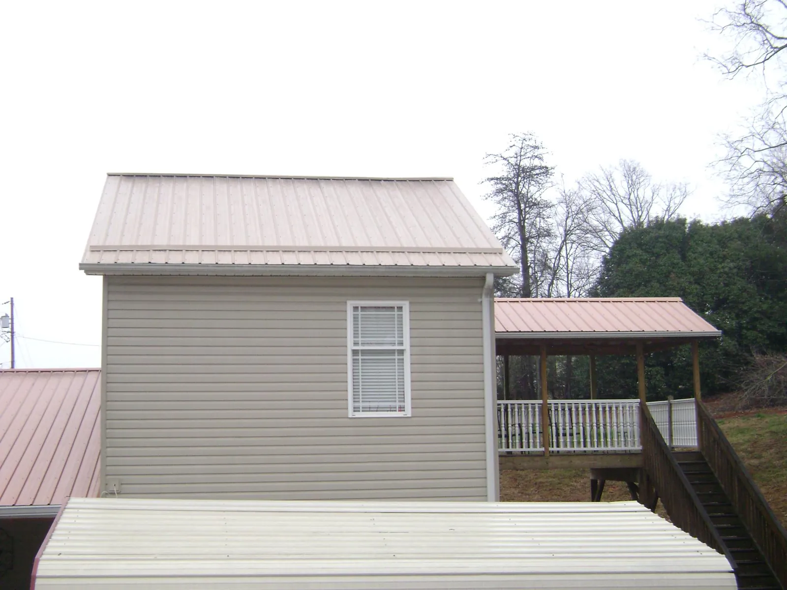 Tan metal roofs on a two story addition and attached porch, from a Roof Replacement job in Manchester